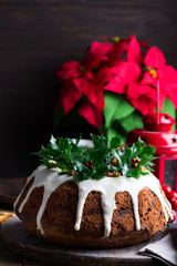Christmas chocolate cake with white icing and pomegranate kernels on a wooden dark background with red lantern and poinsettia