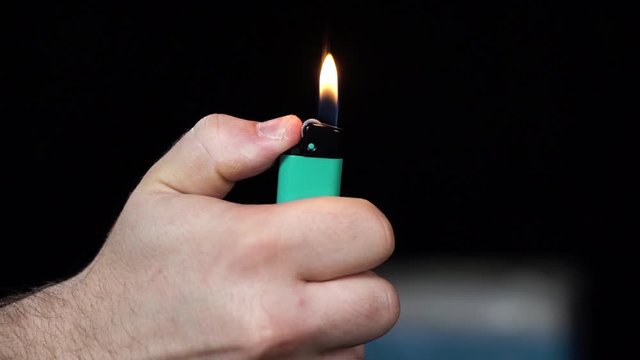 Man hand close up footage of starting fire. Ignition of aquamarine or blue color lighter on black background.