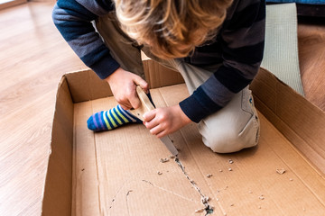 Child playing with a cardboard box and a saw to build.