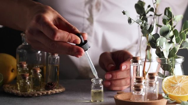 Woman hand pouring eucalyptus essential oil into bottle on grey table