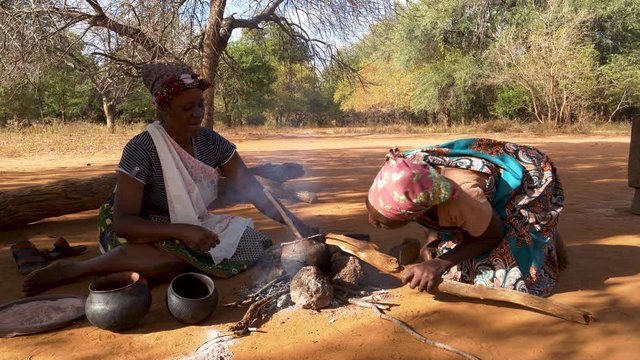 Two woman cooking sorghum in traditional clay pots on a small open fire, Zimbabwe