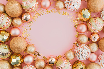 Fototapeta na wymiar Frame made with glitters and golden Christmas tree balls on pale pink background. Festive concept.