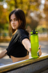 happy athletic woman holding green bottle of water after running in park. focus on bottle