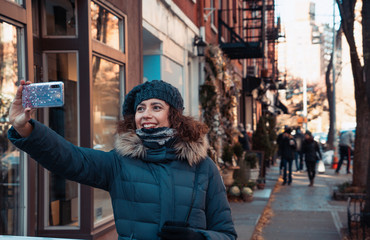 Beautiful curly brunette woman taking selfie self-portrait in Bleecker street, Greenwich Village,...