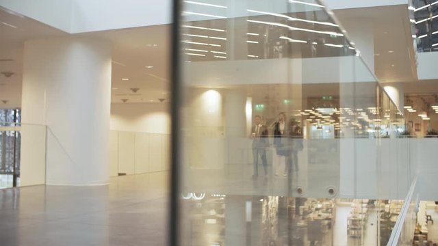 Tracking shot of group of business people of different ethnicities walking through modern office building