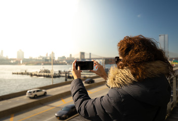 Beautiful curly brunette woman taking selfie self-portrait with the Brookling bridge on the...