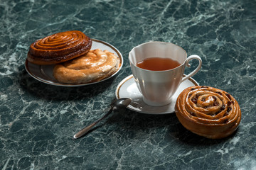 cinnamon bun, Bun with raisins, with saucer, black tea and spoon on background