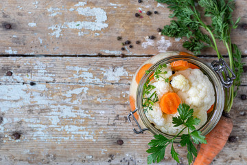 Pickled cauliflower with carrots in a glass jar on an old wooden table. Fermented food. Copy space....