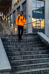african-american man in stylish orange hoodie sweatshirt with backpack goes down stairs