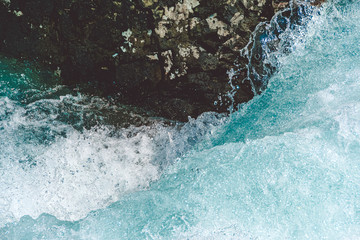 Mountain river with stone in blue water. Turquoise waves of sea tide