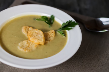 Cream of vegetable soup in a white bowl and spoon on a gray background.