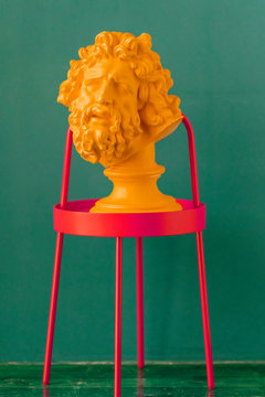 Color plaster head of ancient Greek sculpture on the red metal stand against green wall. Colorful plaser head concept. Hellenistic Period 323 BCE &ndash; 31 CE