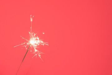 Close up of Brightly burning sparkler on a pink background.