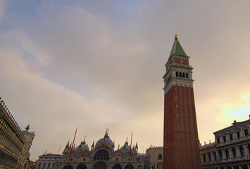 Obraz premium Picturesque landscape view of the high section of The Patriarchal Cathedral Basilica of Saint Mark with red brick tower and other medieval buildings against blue sky. Piazza San Marco, Venice, Italy