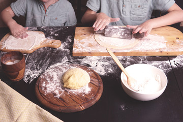   Little kids - boys, brothers making dumplings or ravioli, preparing dough in the kitchen with hands, wooden boards, flour. Child cooking concept. 