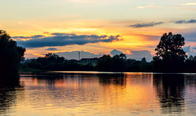 bright summer sunset on a lake with backlit clouds yellow red twilight