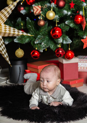 Cute little boy on the floor by the New Year tree.