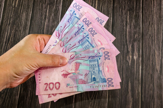 banknotes of 200 hryvnia in hand on a wooden table background.