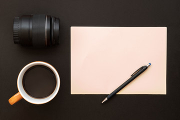 Composition Created Using Coffee cup, Camera Lens, Blank Pink Paper and Black Pencil on Dark Background