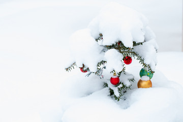 A small Christmas tree is decorated with bright balls. Snowdrifts cover a Christmas tree. Christmas tree on the street after heavy snow
