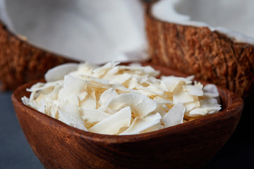 Coconut chips in wooden bowl with two halves of coconut in background.
