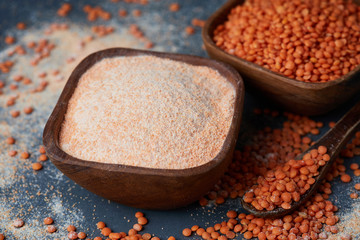 Red lentil flour in wooden bowl on gray background