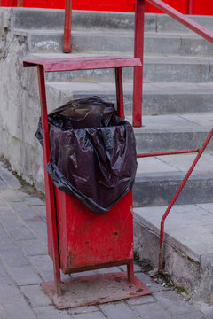 Metal red gerbage bin for rubbish. Public trash can background. Detail of outdoor infrastructure.