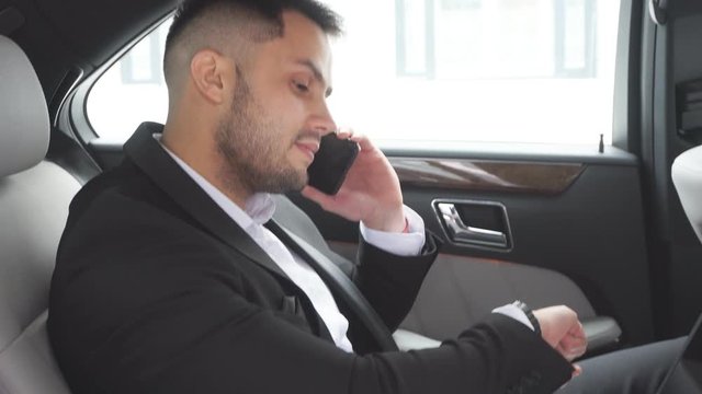 confident businessman looking at wristwatches busy with work, talking with business colleague in executive car