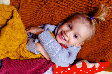 Portrait of a cute little girl in a sweater smiling and lying . Lies in the background of many cozy...