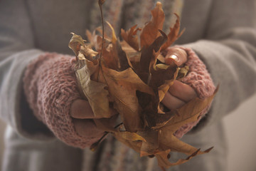 Woman wearing fingerless gloves holding autumn leaves