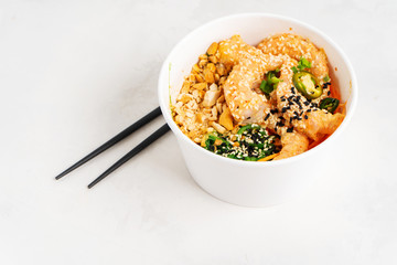 Asian food background with Spicy Shrimp Poke Bowl with rice, seaweeds and sesame seeds, avocado in a lunch box with chopsticks on white. Healthy seafood lunch. Diet food. Top view with copy space.