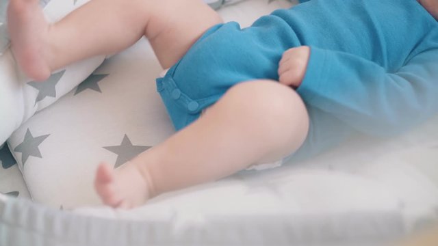 cute little child sucks dummy bothering bare legs in star decorated cocoon in crib under chiffon curtain