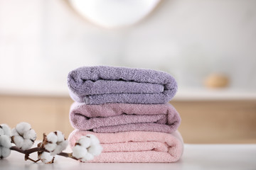 Stack of fresh towels and cotton flowers on table in bathroom
