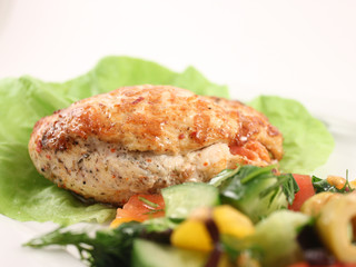 Stuffed chicken breast on lettuce, with fresh vegetable salad, close-up