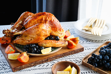 Roasted whole turkey on a table with persimmon, blue grape and lemon for family Thanksgiving...
