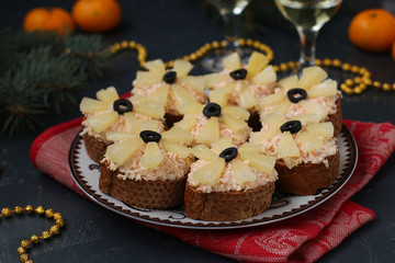 Canapes with cream cheese, crab sticks, black olives and pineapples on dark background, horizontal orientation