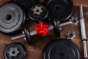 Fototapeta na wymiar gift - dumbbells tied with a red ribbon on a dark wooden table along with sports equipment