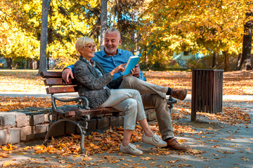 Senior couple enjoying day together while reading book in autumn park