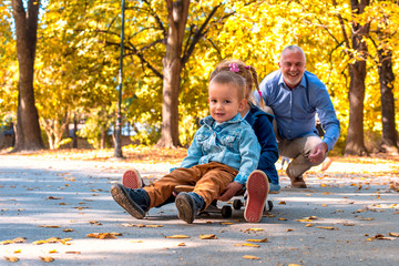 Grandfather enjoying day with her grandchildren in the autumn park while riding skateboard