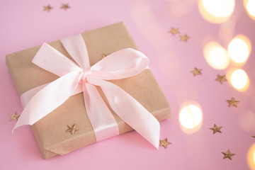 Gift in craft paper with a pink bow on a pink background with holographic sparkles in the form of stars. Template  banner for greeting card your text design 2020. New year, christmas, birthday