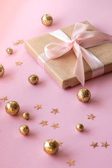 Gift in craft paper with a pink bow on a pink background with gold decorative balls and stars. Template  banner for greeting card your text design 2020. New year, christmas, birthday
