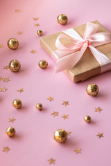 Gift in craft paper with a pink bow on a pink background with gold decorative balls and stars. Template  banner for greeting card your text design 2020. New year, christmas, birthday