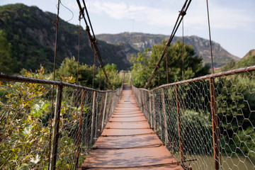 Fototapeta na wymiar front view of a narrow hung steel bridge over a river at nature