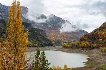 An autumn landscape with a stone bridge across the lake in a mountain valley. Autumn paints of nature in the mountains with clouds and a stone bridge over the river from a mountain lake.