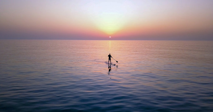 SUP Surfing on amazing sea sunset.  Image of Stand Up Paddle Board Man Silhouette on Amazing Sunset over Sea. Standup Paddle Boarding.