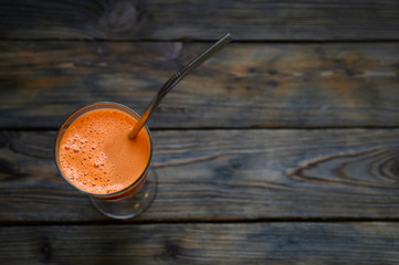 orange carrot freshly squeezed juice in a glass goblet and with a reusable metal drinking straw on a dark wooden background. flat lay, top view, space for text
