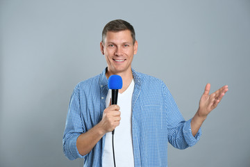 Male journalist with microphone on grey background