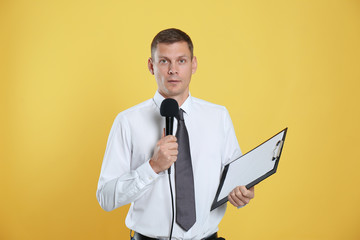 Male journalist with microphone and clipboard on yellow background
