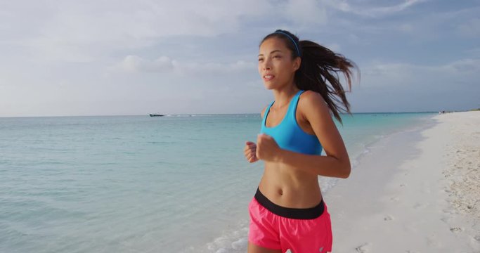 Exercising young woman runner jogging and running on beach happy living healthy aspirational fitness lifestyle. Sporty young Asian Caucasian female in sportswear. SLOW MOTION STEADICAM RED Camera