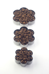  three flower-shaped containers filled with coffee beans and standing in a row one after another on a white background